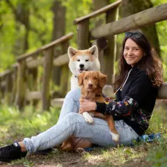Kobieta z dwoma psami w lesie. Jeden piesek jest na jej kolanach, drugi za nim. Wskazówki, jak uspokoić sukę podczas cieczki, mogą być pomocne.