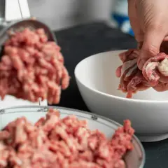 Ręka wrzuca mięso do maszynki, przygotowując pyszne serca dla psa.