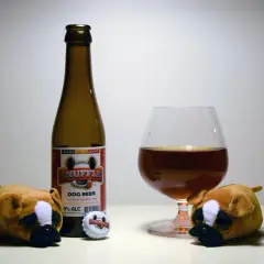 Dwa pluszowe pieski patrzą na butelkę piwa "Snuffle Dog Beer" i kieliszek. Czy pies może pić piwo? To piwo jest dla psów, 0% alkoholu.