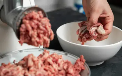 Ręka wrzuca mięso do maszynki, przygotowując pyszne serca dla psa.