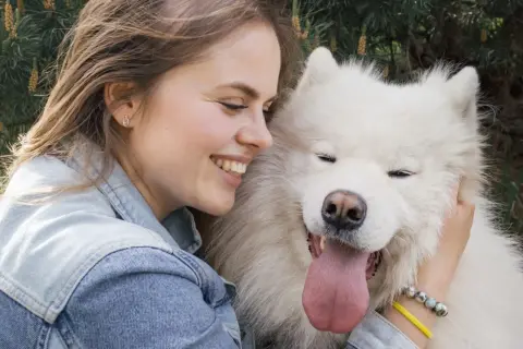 Uśmiechnięta dziewczyna przytula swojego białego psa. To prawdziwy psi tłumacz, który rozumie każde jej słowo.