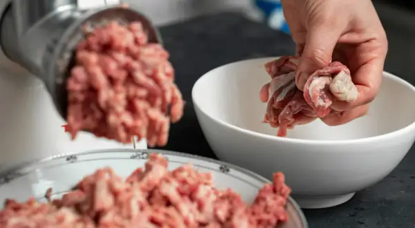Ręka wrzuca mięso do maszynki, przygotowując pyszne serca dla psa.