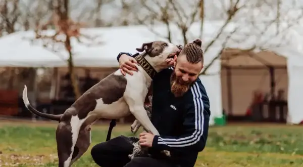 Mężczyzna z brodą i warkoczami przytula psa. Pies ma obrożę z napisem "Jordan". Szukając imiona dla psa, warto inspirować się tym, co kochamy.