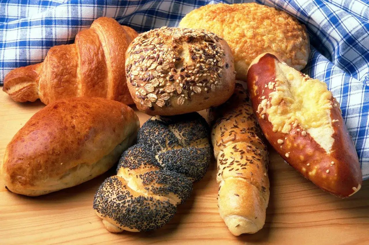 Różnorodne pieczywo: croissant, bułka z ziarnami, chleb z makiem, bułka z kminkiem i precel z serem. Czy pies może jeść chleb? Lepiej nie ryzykować.